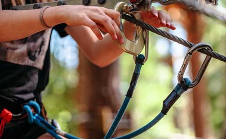 Bilden visar en närbild på en beskuren person iförd utrustning för Acropark i närbild syns händerna som håller linan.