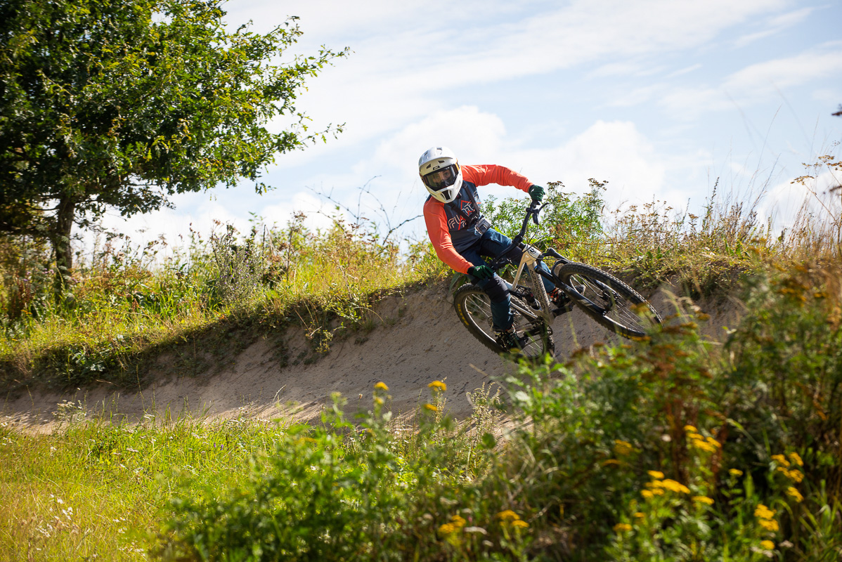 Cyklist som cyklar i Bike Park, i förgrunden syns grönskande blommor och himlen är blå.