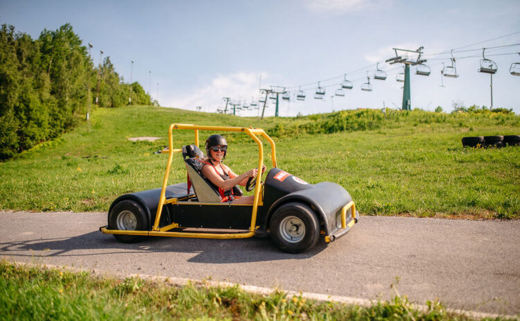 Bilden visar Flottsbro Downhill Cars, aktivitet med gokart sedd från sidan kör på en väg i en backe med grönt gräs och blå himmel bakom.
