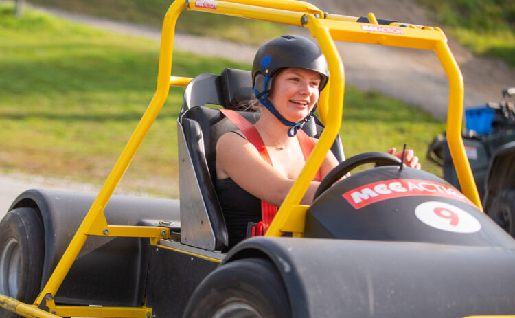 En ung tjej sedd snett framifrån som kör Flottbros Downhill Cars, hon bär hjälm och ler.