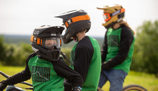 Tre barn/ungdomar med hjälpar och cyklar, barnet närmast i bild är vänd mot kameran