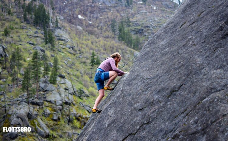 Bilden visar en person som klättrar upp för en klippa i bakgrunden syns skog.