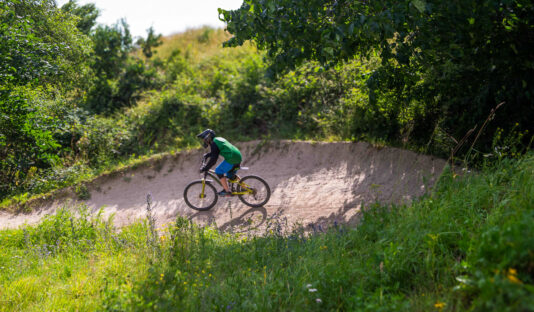 Bild på på ett grönskande landskap och en cykelbana med en cyklist sedd på långt avstånd