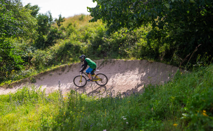Bild på på ett grönskande landskap och en cykelbana med en cyklist sedd på långt avstånd
