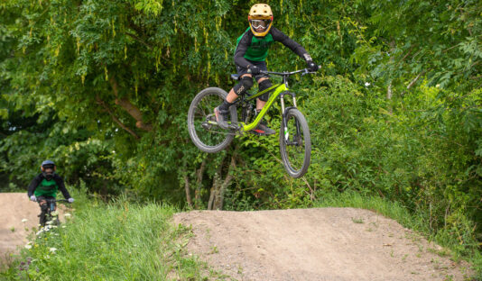 En cyklist som gör ett hopp med cykeln i bakgrunden syns lummig grönska