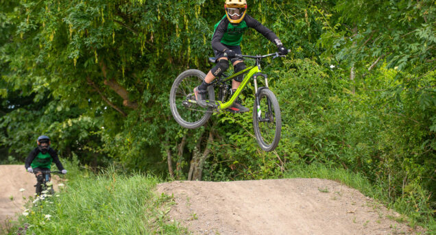 En cyklist som gör ett hopp med cykeln i bakgrunden syns lummig grönska