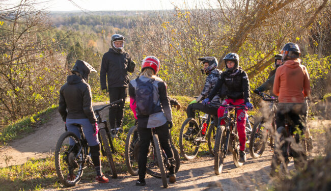 5 cyklister sedda bakifrån med en ledare sedd bakifrån ståendes på en höjd