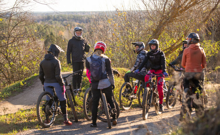 5 cyklister sedda bakifrån med en ledare sedd bakifrån ståendes på en höjd