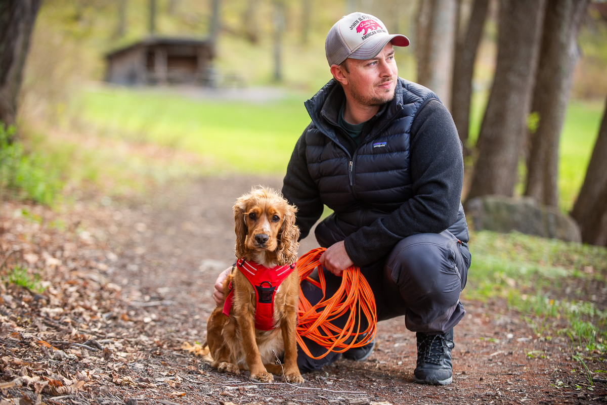 porträtt på en person och en hund på promenad i skogen.