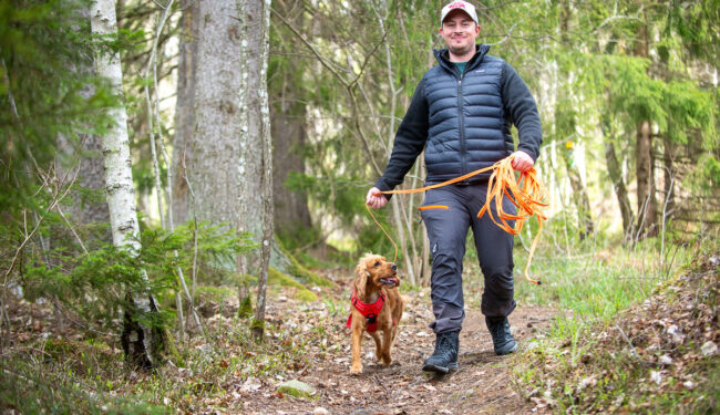 Bilden visar en person och en hund på promenad i skogen.