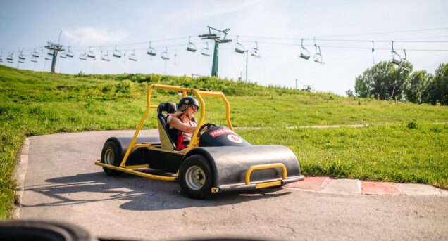 En kvinna kör en Downhill Car ner för en backe under sommaren.