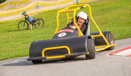 En ung tjej kör downhill car – en go cart-liknande bil – ner för skidbacken under sommaren.