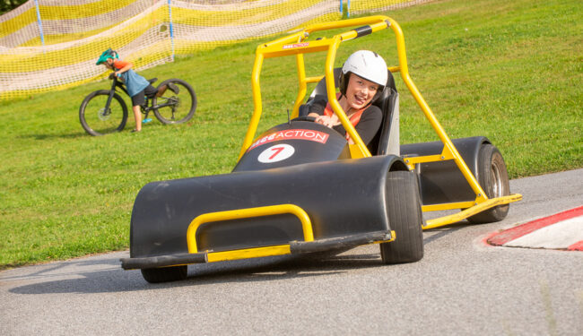 En ung tjej kör downhill car – en go cart-liknande bil – ner för skidbacken under sommaren.