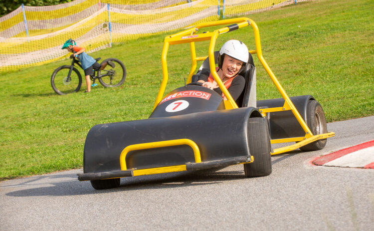 En ung tjej kör downhill car – en go cart-liknande bil – ner för skidbacken under sommaren.
