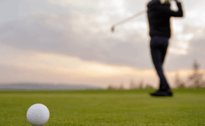 närbild på golfboll med en spelare i siluett på en green.