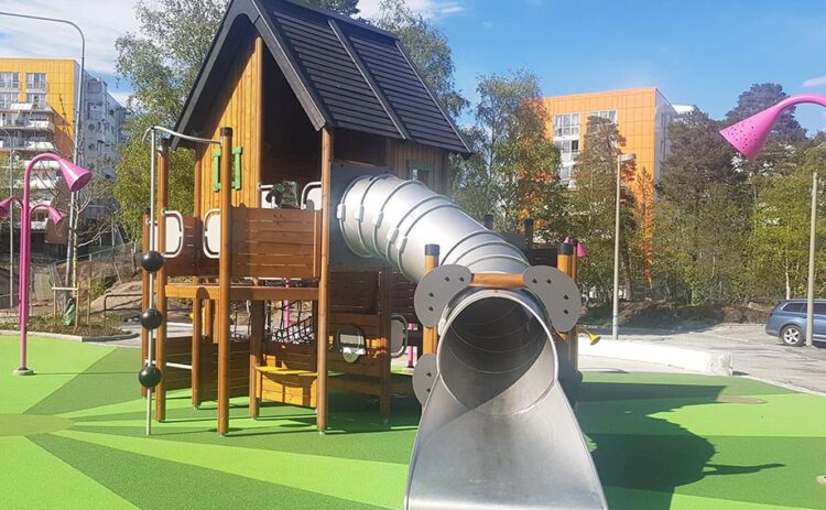 bild på Flemmingsbergsparken i Huddinge, en lfärgglad lekställning och grönt gräs mot blå himmel.