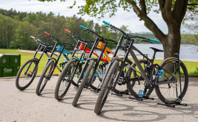 Bild på en rad downhill-syklar, i bakgrunden syns en sjö och ett stort träd.