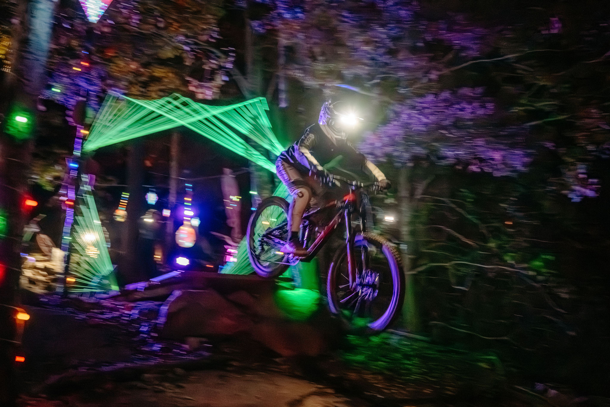 En cyklist med en pannlampa som cyklar i en bike park under ett kvällsevent.
