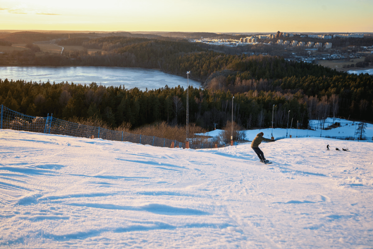 Vy över Familjebacken på Flottsbro med en snowboard-åkare i vårsolen. 