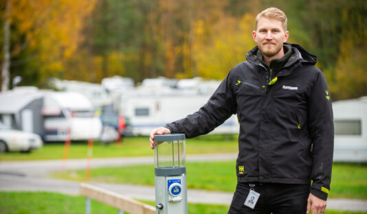 bilden visar en man, i bakgrunden syns grön yta och husvagnar på en camping